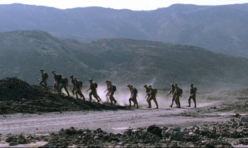 Movie still from “Beau Travail” (1999), directed by Claire Denis – A group of men walking across a dirt field; Extreme Wide shot, Low angle