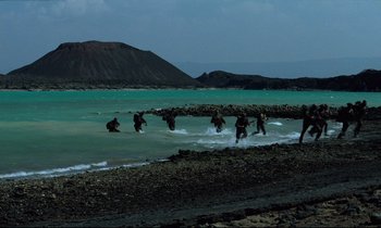 Movie still from “Beau Travail” (1999), directed by Claire Denis – A group of people wading through the water; Extreme Wide shot, High angle