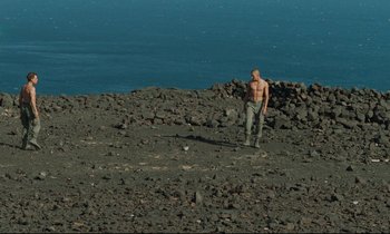 Movie still from “Beau Travail” (1999), directed by Claire Denis – A man standing on top of a rocky hill; Wide shot, High angle