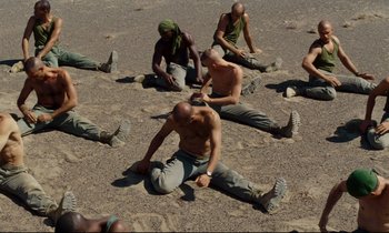 Movie still from “Beau Travail” (1999), directed by Claire Denis – A group of men sitting on the ground in the sand; Wide shot, High angle