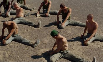 Movie still from “Beau Travail” (1999), directed by Claire Denis – A group of men sitting on top of a sandy beach; Wide shot, Overhead angle
