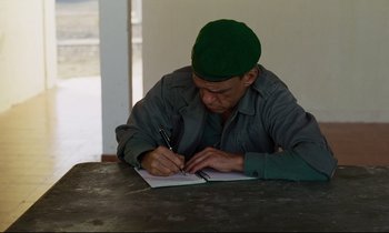 Movie still from “Beau Travail” (1999), directed by Claire Denis – A man writing on a piece of paper with a pen; Medium shot, High angle