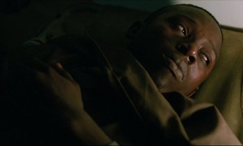 Movie still from “Beau Travail” (1999), directed by Claire Denis – A man laying in a bed in a dark room; Close Up shot, High angle