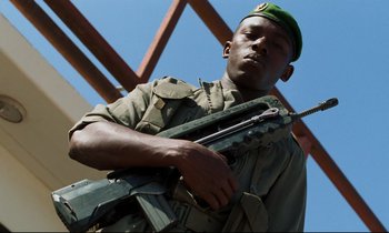 Movie still from “Beau Travail” (1999), directed by Claire Denis – A man in a green hat holding a rifle; Medium shot, Low angle