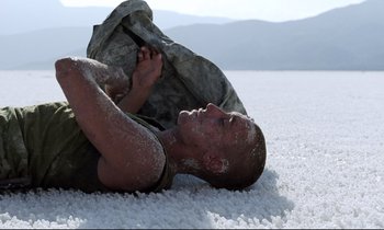 Movie still from “Beau Travail” (1999), directed by Claire Denis – A man laying on the ground covered in snow; Medium shot, Low angle