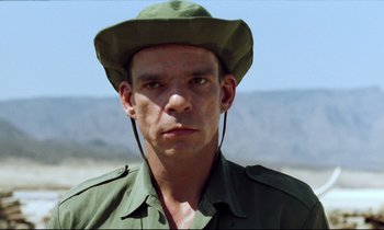Movie still from “Beau Travail” (1999), directed by Claire Denis – A person wearing a hat; Close Up shot, Over the shoulder angle