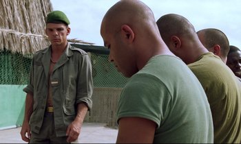 Movie still from “Beau Travail” (1999), directed by Claire Denis – A man in a green hat is talking to two other men; Medium shot, Over the shoulder angle