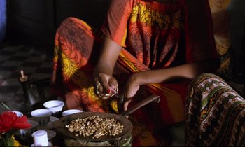 Movie still from “Beau Travail” (1999), directed by Claire Denis – A woman in an orange and yellow dress preparing food on top of a pan; Medium shot, Overhead angle