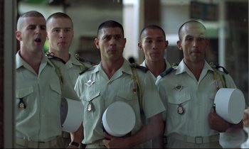 Movie still from “Beau Travail” (1999), directed by Claire Denis – A group of men standing next to each other holding hats; Medium shot, Low angle