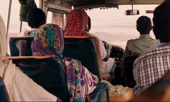 Movie still from “Beau Travail” (1999), directed by Claire Denis – A group of people sitting in a bus with luggage; Medium shot, Over the shoulder angle