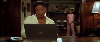 Movie still from “Beauty Shop” (2005), directed by Bille Woodruff – A woman sitting in front of an open laptop computer; Medium shot, Over the shoulder angle