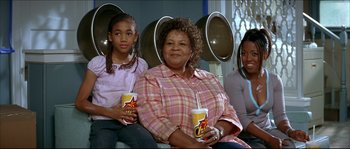 Movie still from “Beauty Shop” (2005), directed by Bille Woodruff – A woman sitting next to two young girls holding drinks; Medium shot, High angle