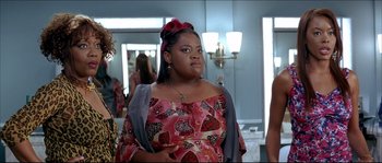 Movie still from “Beauty Shop” (2005), directed by Bille Woodruff – A woman in a pink and red dress standing next to a mirror; Medium shot, Over the shoulder angle