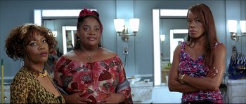 Movie still from “Beauty Shop” (2005), directed by Bille Woodruff – A woman in a red and white dress standing in a bathroom; Medium shot, Over the shoulder angle