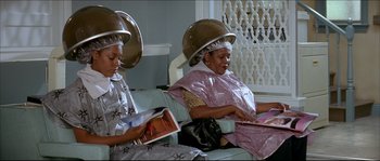 Movie still from “Beauty Shop” (2005), directed by Bille Woodruff – Two women sitting down with their hair dryers on their heads; Medium shot, High angle