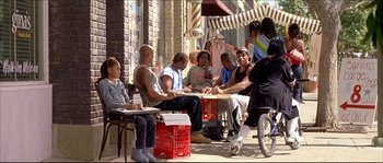Movie still from “Beauty Shop” (2005), directed by Bille Woodruff – A group of people sitting around a table on a sidewalk; Wide shot, Over the shoulder angle