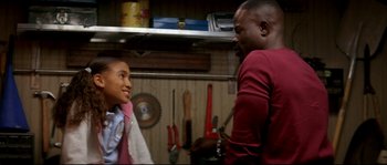 Movie still from “Beauty Shop” (2005), directed by Bille Woodruff – A man standing next to a young boy in a garage; Medium shot, Over the shoulder angle