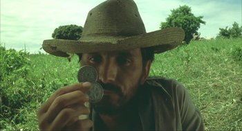 Movie still from “Before Night Falls” (2000), directed by Julian Schnabel – A man wearing a straw hat holding two coins; Close Up shot, Low angle
