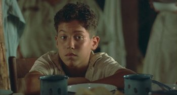 Movie still from “Before Night Falls” (2000), directed by Julian Schnabel – A young man sitting at a table in front of a plate of food; Close Up shot, Over the shoulder angle