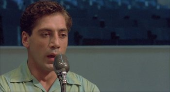 Movie still from “Before Night Falls” (2000), directed by Julian Schnabel – A man is speaking into a microphone in front of a crowd; Close Up shot, Low angle