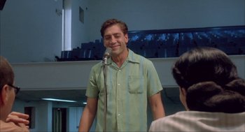 Movie still from “Before Night Falls” (2000), directed by Julian Schnabel – A man standing in front of a microphone in a room; Medium shot, Low angle