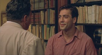 Movie still from “Before Night Falls” (2000), directed by Julian Schnabel – Two men standing next to each other in front of a book shelf; Close Up shot, Over the shoulder angle