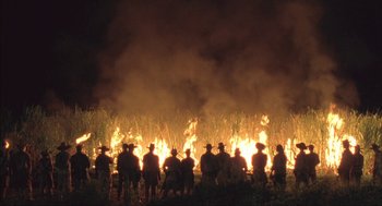 Movie still from “Before Night Falls” (2000), directed by Julian Schnabel – A group of people standing in front of a burning field; Extreme Wide shot, Low angle