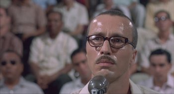Movie still from “Before Night Falls” (2000), directed by Julian Schnabel – A man with a mustache is holding a microphone in front of a group of people; Close Up shot, Low angle