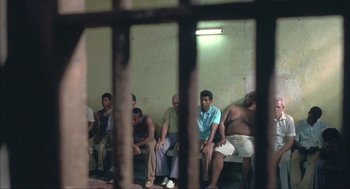 Movie still from “Before Night Falls” (2000), directed by Julian Schnabel – A group of men sitting next to each other in a room; Wide shot, High angle