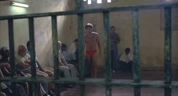 Movie still from “Before Night Falls” (2000), directed by Julian Schnabel – A man in a red swim suit standing in front of a group of people; Wide shot, High angle