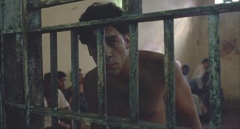 Movie still from “Before Night Falls” (2000), directed by Julian Schnabel – A shirtless man behind bars in a jail cell; Close Up shot, Low angle