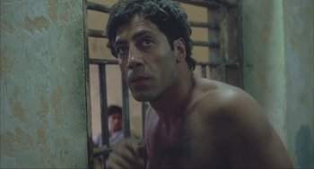 Movie still from “Before Night Falls” (2000), directed by Julian Schnabel – A shirtless man in a jail cell looking at the camera; Close Up shot, Low angle