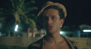 Movie still from “Before Night Falls” (2000), directed by Julian Schnabel – A man wearing a straw hat is standing in the dark; Close Up shot, Over the shoulder angle