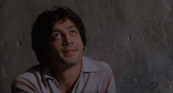 Movie still from “Before Night Falls” (2000), directed by Julian Schnabel – A person sitting in front of a brick wall; Close Up shot, Low angle