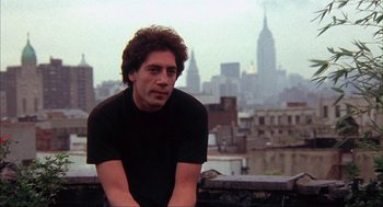 Movie still from “Before Night Falls” (2000), directed by Julian Schnabel – A man sitting on top of a building in front of a city skyline; Close Up shot, Low angle