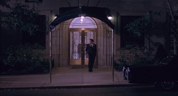 Movie still from “Before Night Falls” (2000), directed by Julian Schnabel – A man standing in front of an entrance to a building at night; Wide shot, Low angle