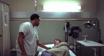 Movie still from “Before Night Falls” (2000), directed by Julian Schnabel – A man standing next to a woman in a hospital bed; Medium shot, High angle