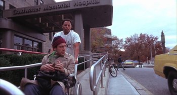 Movie still from “Before Night Falls” (2000), directed by Julian Schnabel – A man riding a bike next to another man in front of a building; Wide shot, Low angle
