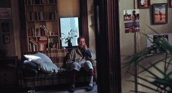 Movie still from “Before Night Falls” (2000), directed by Julian Schnabel – A man sitting on top of a couch next to a window; Wide shot, High angle