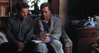 Movie still from “Before Night Falls” (2000), directed by Julian Schnabel – Two men sitting on a couch looking at a book; Medium shot, Over the shoulder angle