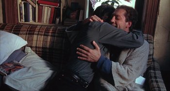 Movie still from “Before Night Falls” (2000), directed by Julian Schnabel – Two people hugging each other in a living room; Medium shot, Over the shoulder angle