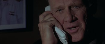 Movie still from “Behind Enemy Lines” (2001), directed by John Moore – An older man talking on a phone while holding his hand up to his ear; Close Up shot, Low angle