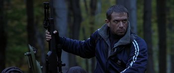 Movie still from “Behind Enemy Lines” (2001), directed by John Moore – A man holding a rifle in a forest; Medium shot, Low angle