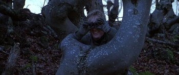 Movie still from “Behind Enemy Lines” (2001), directed by John Moore – A person in the woods looking through binoculars; Medium shot, Low angle