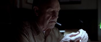 Movie still from “Behind Enemy Lines” (2001), directed by John Moore – An older man smoking a cigarette while looking at a phone; Close Up shot, Low angle