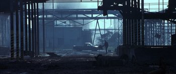 Movie still from “Behind Enemy Lines” (2001), directed by John Moore – A man standing next to an old car in an industrial setting; Extreme Wide shot, Low angle