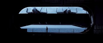 Movie still from “Behind Enemy Lines” (2001), directed by John Moore – A man standing on the deck of an aircraft carrier looking out over the water; Wide shot, Low angle