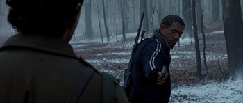 Movie still from “Behind Enemy Lines” (2001), directed by John Moore – A man holding a gun while standing next to another man in the woods; Medium shot, Over the shoulder angle