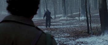 Movie still from “Behind Enemy Lines” (2001), directed by John Moore – A man with a rifle walking through the woods; Wide shot, Over the shoulder angle
