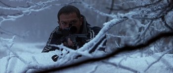 Movie still from “Behind Enemy Lines” (2001), directed by John Moore – A man is holding a rifle in a snowy forest; Medium shot, Low angle